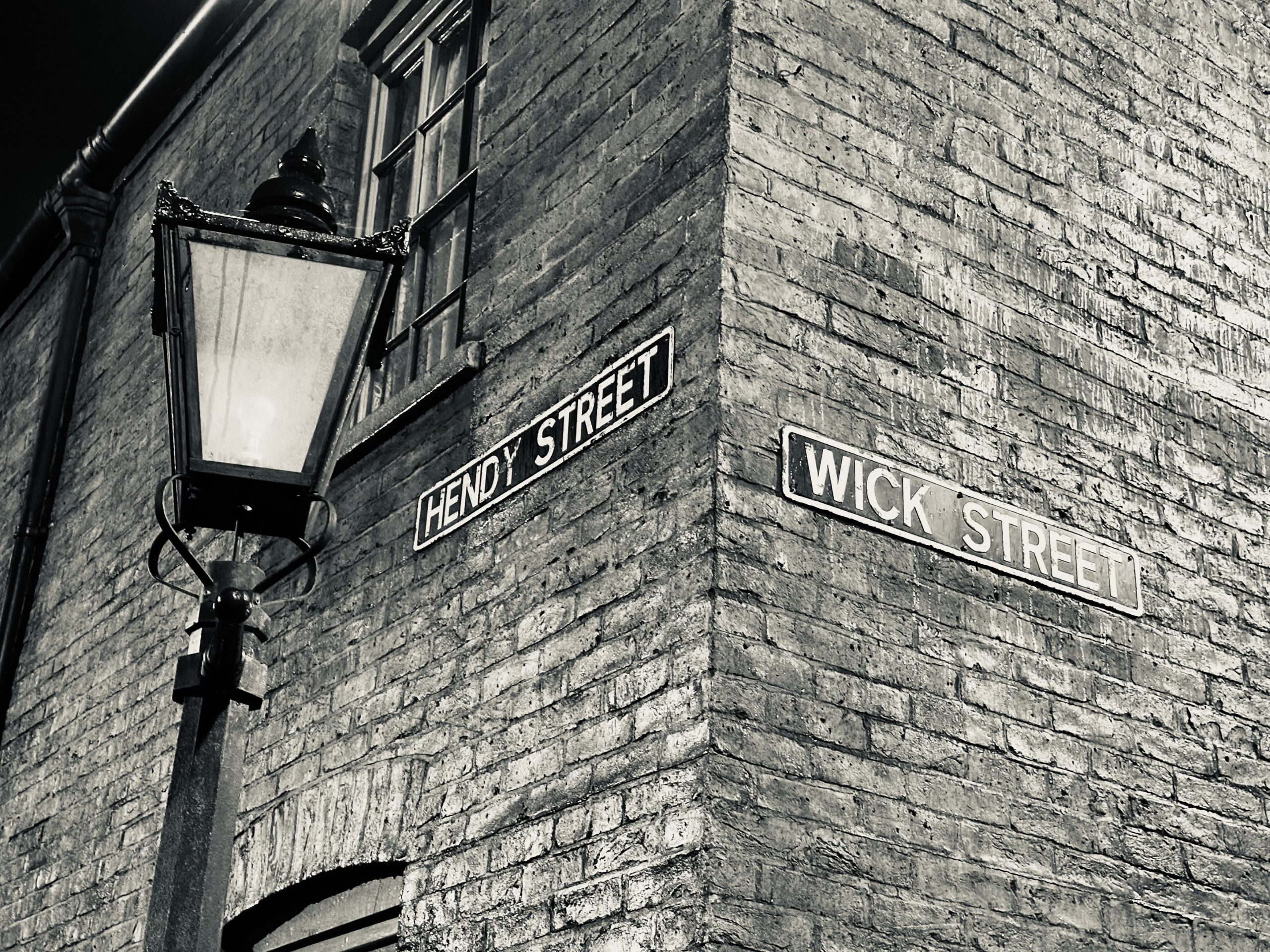 Hendy Street and Wick Street signs on a brick corner beside a gas lamp